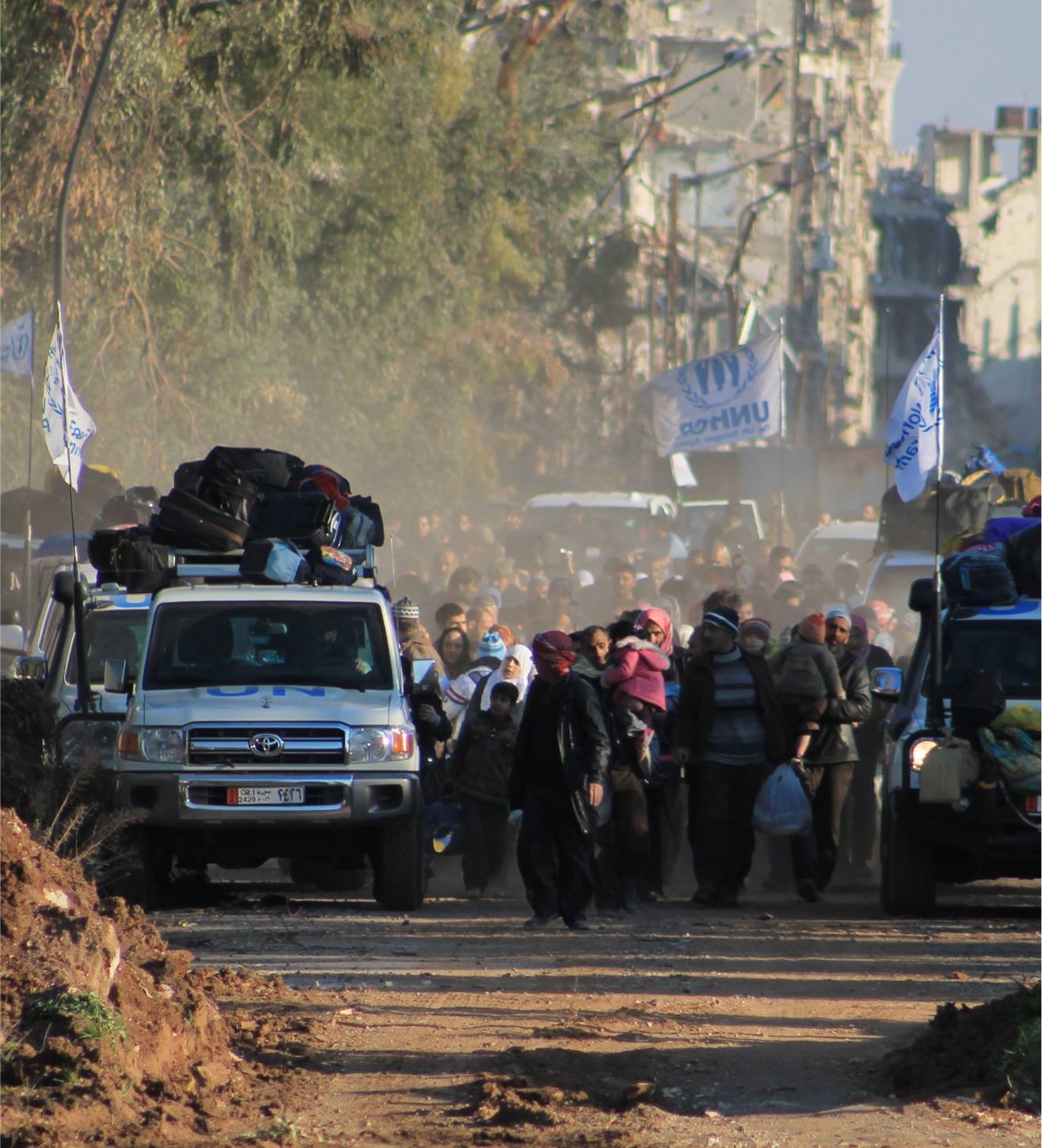 Families and vehicles moving through a war-damaged city